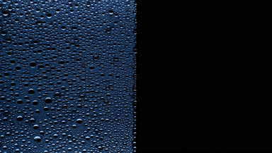 Blue water drops blown off the wet glass surface on black bg