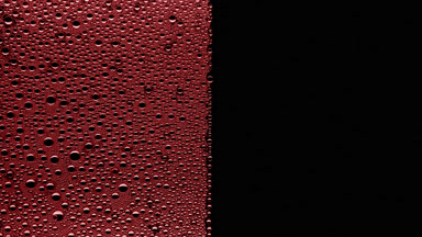 Pink water drops blown off the wet glass surface on black bg