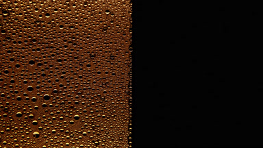 Yellow water drops blown off the wet glass surface on black bg