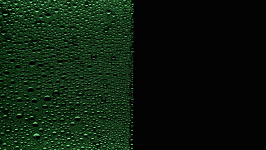Green water drops blown off the wet glass surface on black bg