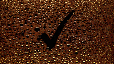 Orange checkmark sign blown off the wet glass on black bg