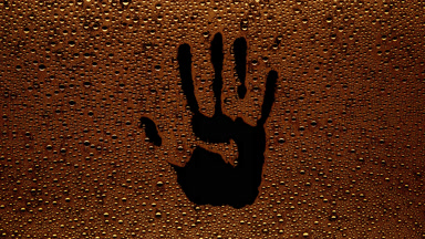 Orange handprint blown off the wet glass on black background