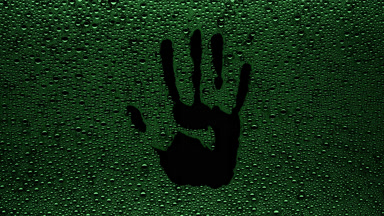 Green handprint blown off the wet glass on black background