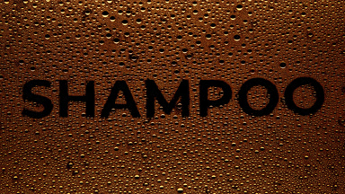 Orange shampoo text blown off the wet glass on black background
