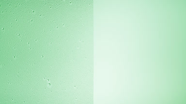 Drops are being blown off the half of the wet glass on a green bg