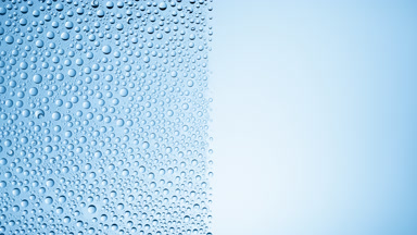 Drops are being blown off the half of the wet glass on a blue bg