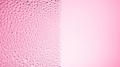 Drops are being blown off the half of the wet glass on a pink bg