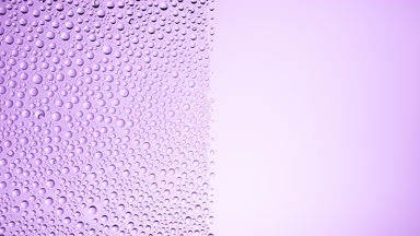 Drops are being blown off the half of the wet glass on a purple bg