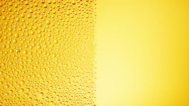 Drops are being blown off the half of the wet glass on a yellow bg