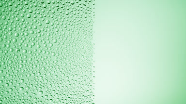 Drops are being blown off the half of the wet glass on a green bg