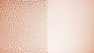 Drops are being blown off the half of the wet glass on a purple bg