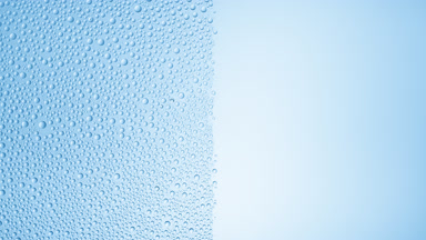 Drops are being blown off the half of the wet glass on a beige bg