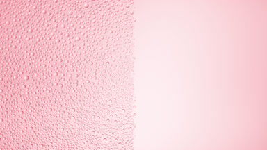 Drops are being blown off the half of the wet glass on a pink bg
