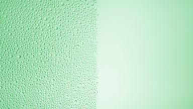 Drops are being blown off the half of the wet glass on a green bg