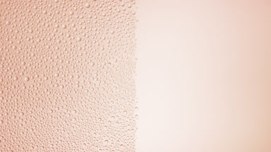Drops are being blown off the half of the wet glass on a beige bg