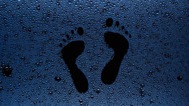 Blue footprints blown off the wet glass on black background