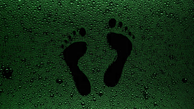 Green footprints blown off the wet glass on black background