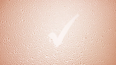Checkmark blown off the wet glass on beige background