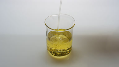 Yellow oil being poured into empty beaker on grey background