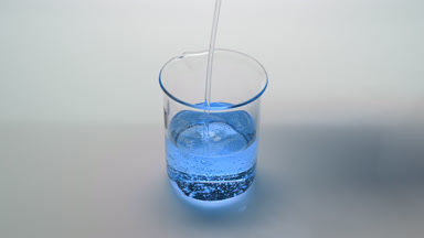 Cyan oil being poured into empty beaker on grey background