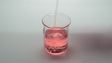 Pink oil being poured into empty beaker on grey background