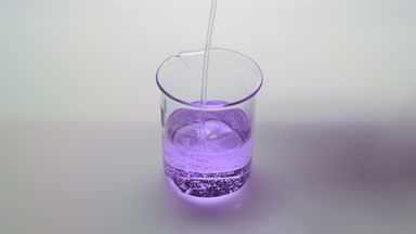 Purple oil being poured into empty beaker on grey background