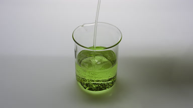 Green oil being poured into empty beaker on grey background