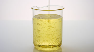 Oil being poured into beaker with yellow oil on grey background