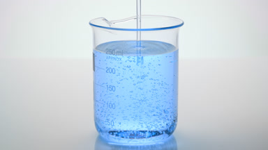 Oil being poured into beaker with blue oil on grey background
