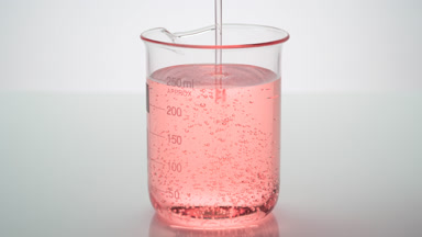 Oil being poured into beaker with rose oil on grey background