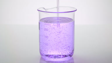 Oil being poured into beaker with violet oil on grey background