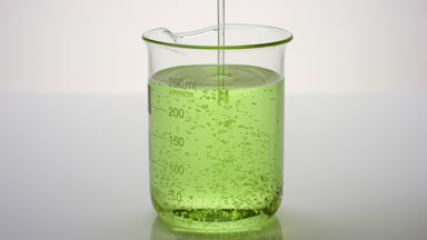 Oil being poured into beaker with green oil on grey background