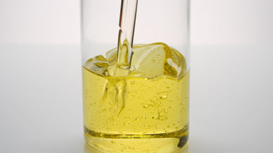 Sunflower oil being poured into empty beaker on grey background