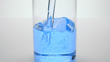 Blue oil being poured into empty beaker on grey background