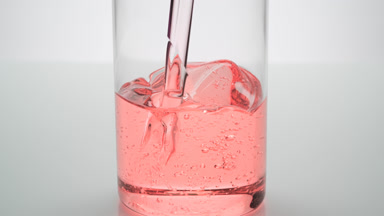 Rose oil being poured into empty beaker on grey background