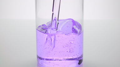 Lavender oil being poured into empty beaker on grey background