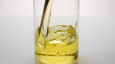 Olive oil is being poured into empty beaker on grey background