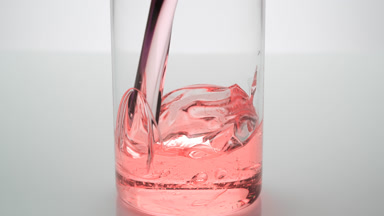 Rosehip oil is being poured into empty beaker on grey background