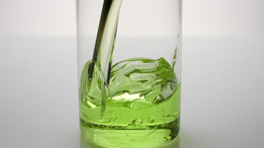 Green tea oil being poured into empty beaker on grey background