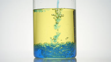 Blue oil is being poured into beaker with blue and yellow oils
