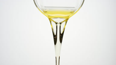 Yellow oil is being poured from beaker on grey background