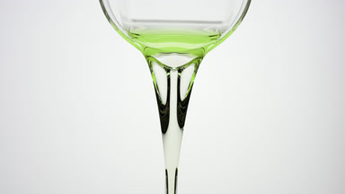 Green oil is being poured from beaker on grey background