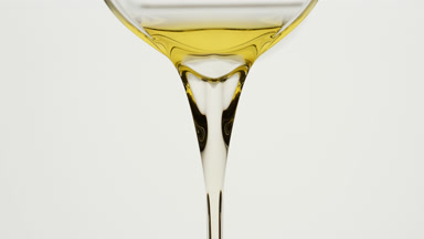 Carrot oil is being poured from beaker on grey background