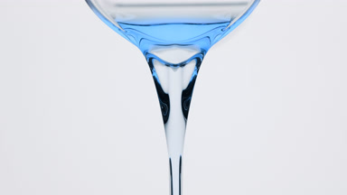 Blue tansy oil is being poured from beaker on grey background
