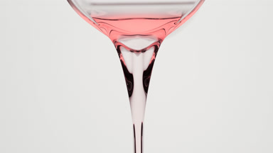 Macro of rose oil being poured from beaker on grey background