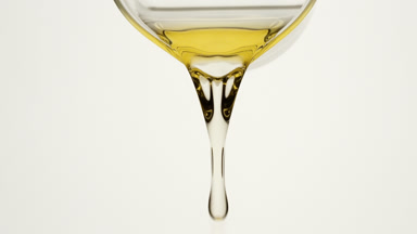 Chamomile oil is being poured from beaker on grey background