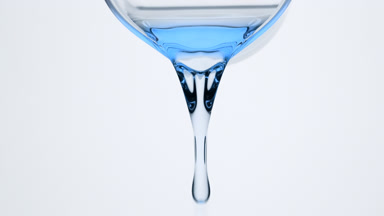 Macro of cyan oil is being poured from beaker on grey background
