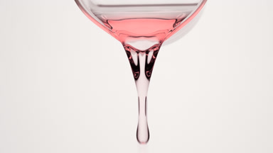 Pale pink oil is being poured from beaker on grey background