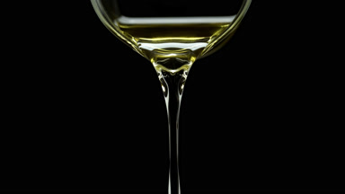 Jojoba oil is being poured from beaker on black background