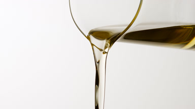 Almond oil is being poured from beaker on grey background